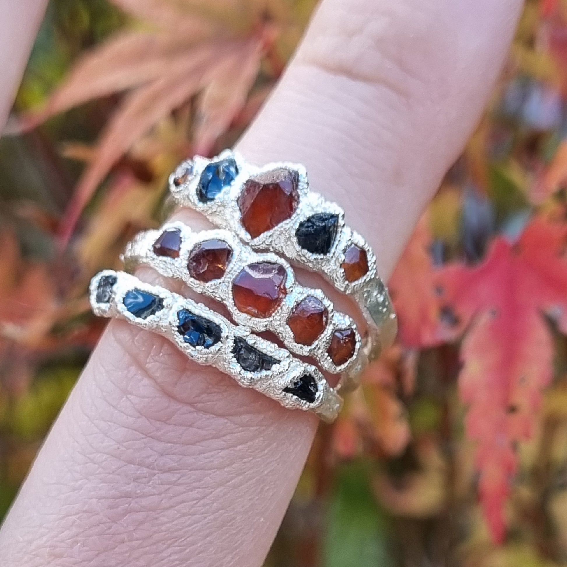Stack of silver rings with brown and black gemstones on a finger against a blurred natural background