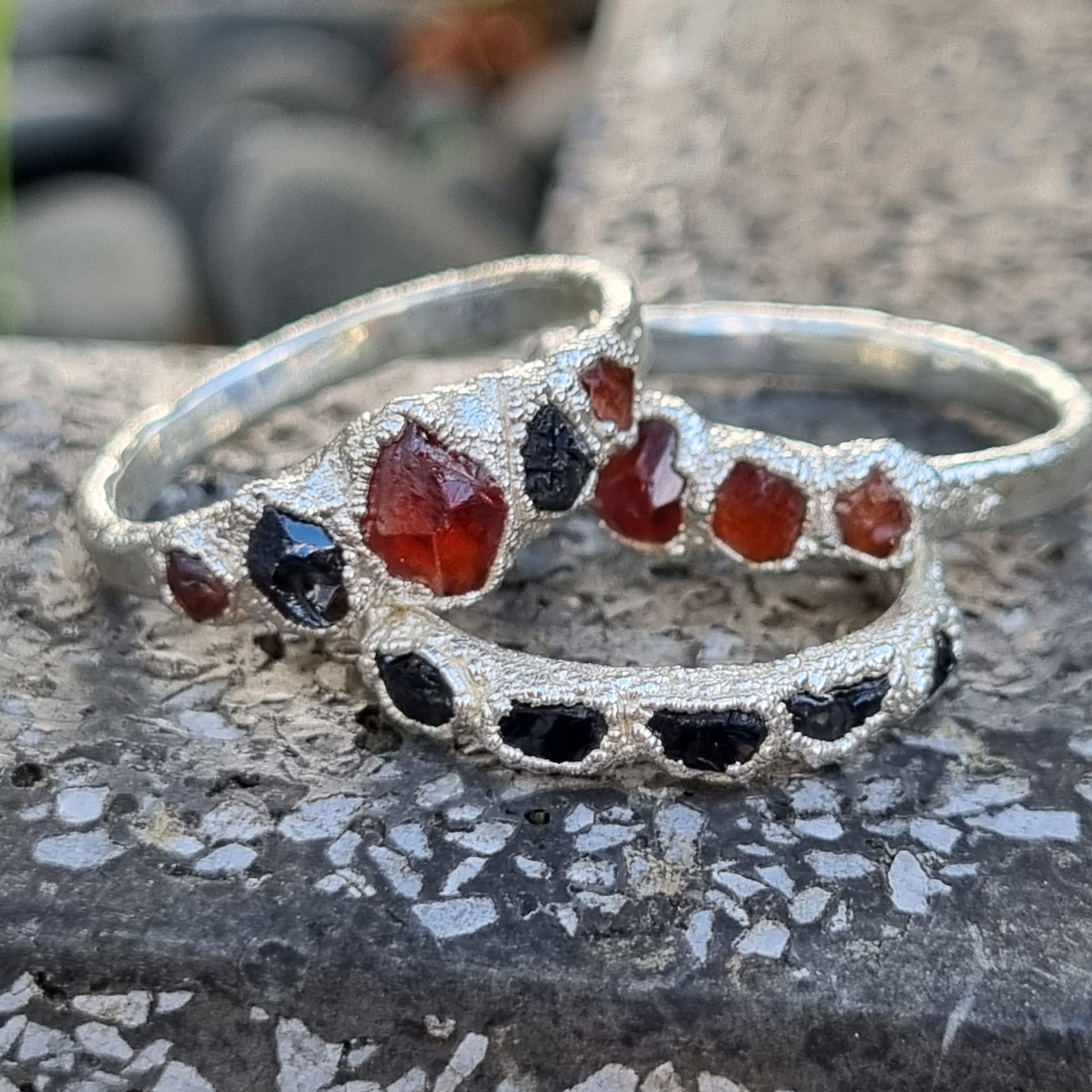 Rustic sterling silver rings with orange and black gemstones on a stone surface