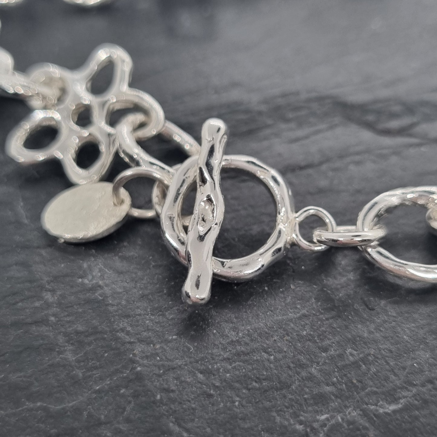 Close-up of a sterling silver necklace fastening toggle on a dark textured background