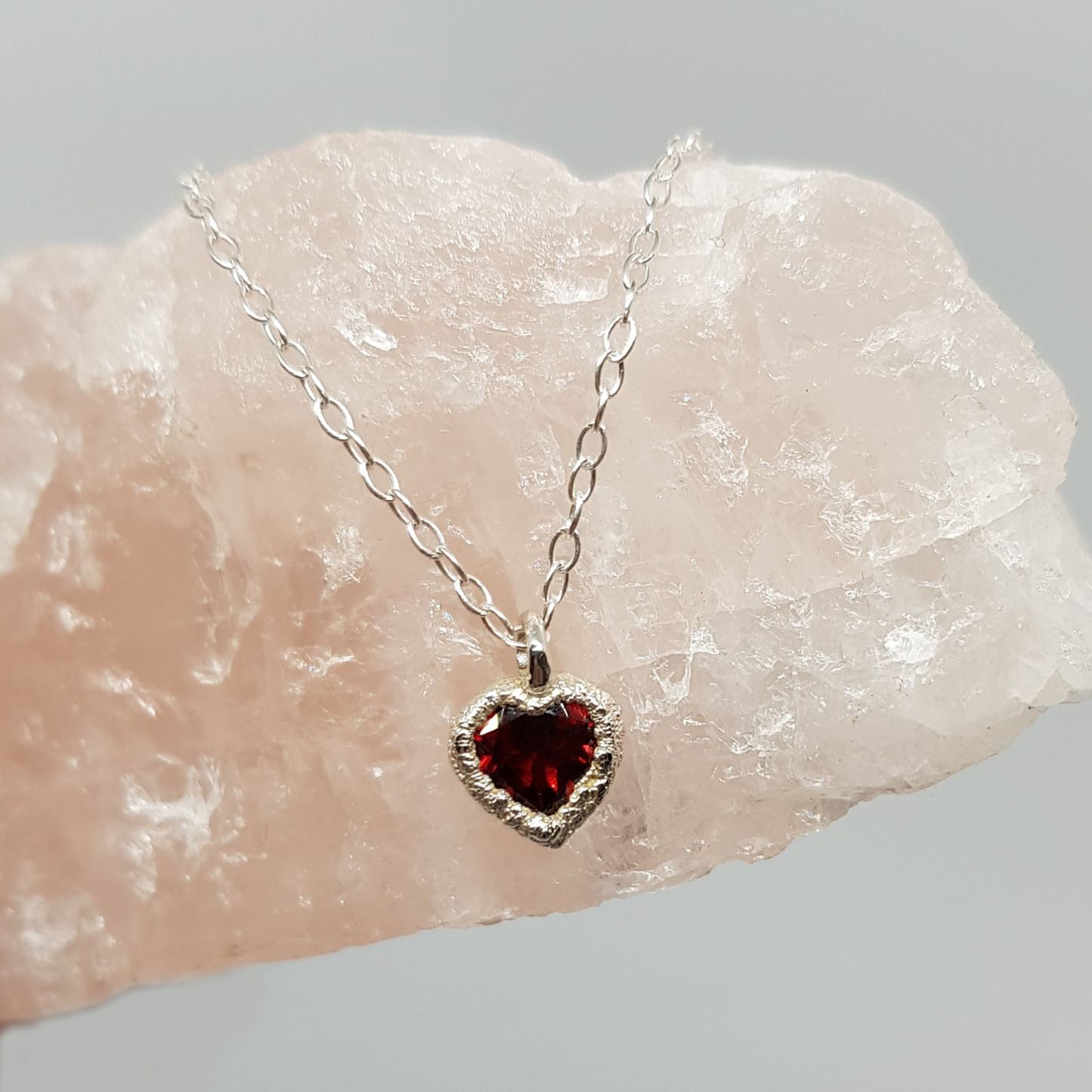 raw silver garnet heart silver necklace displayed on a piece of rose quartz