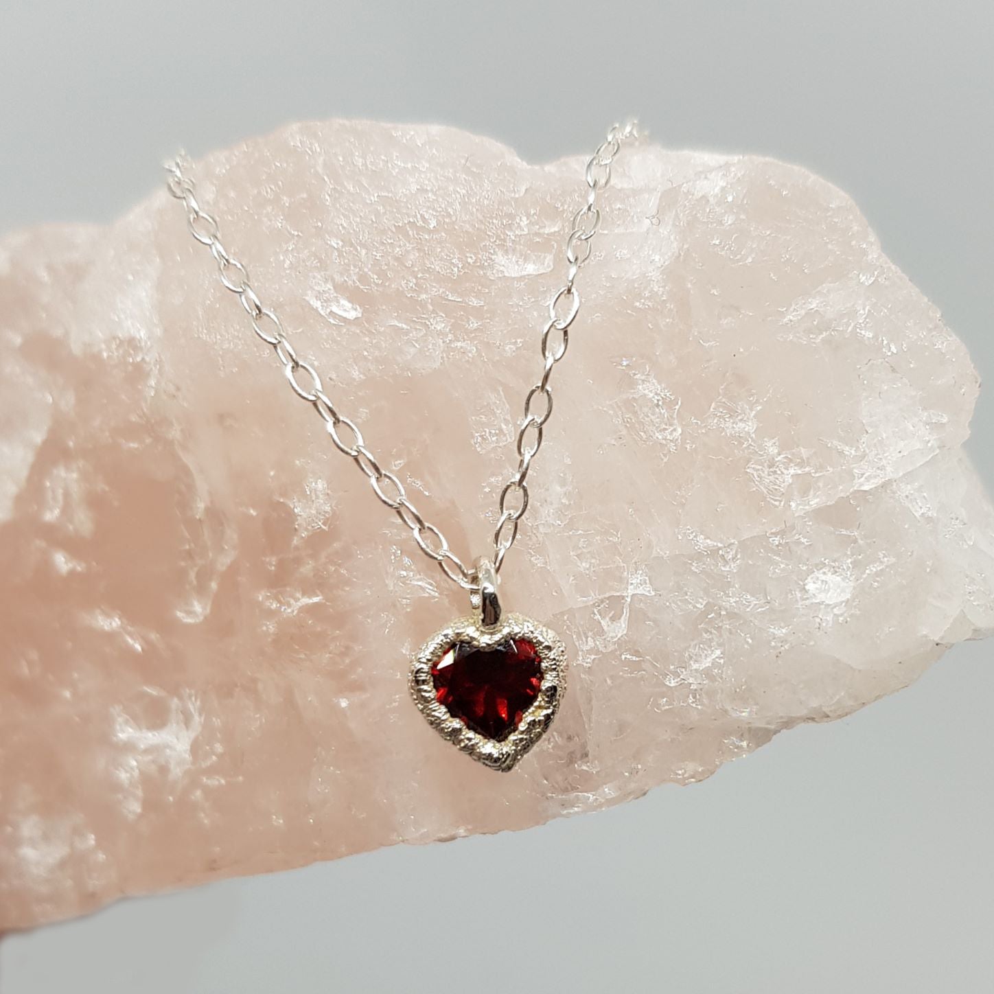 raw silver garnet heart silver necklace displayed on a piece of rose quartz