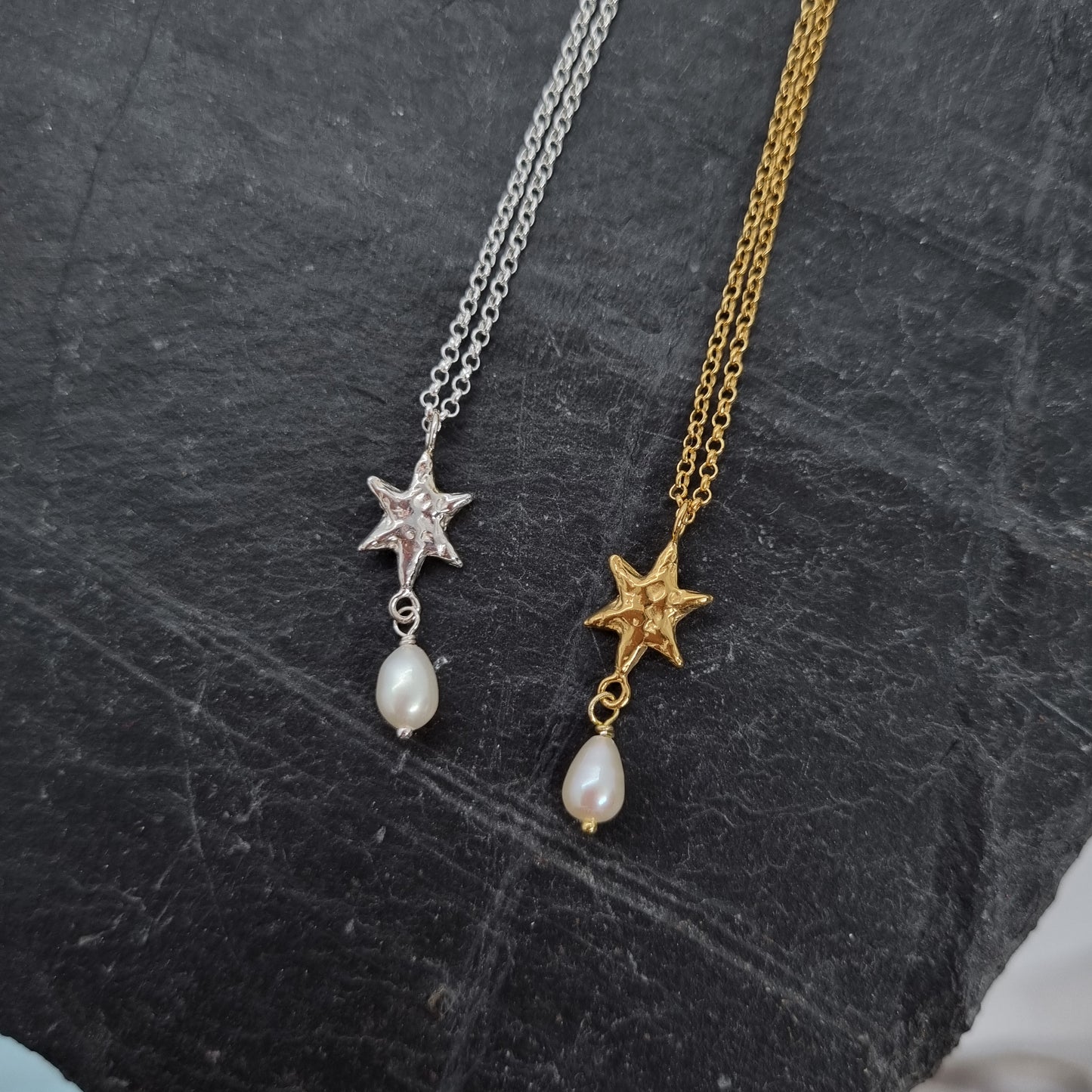 Two star-shaped pendants on gold and silver chains against a dark textured background