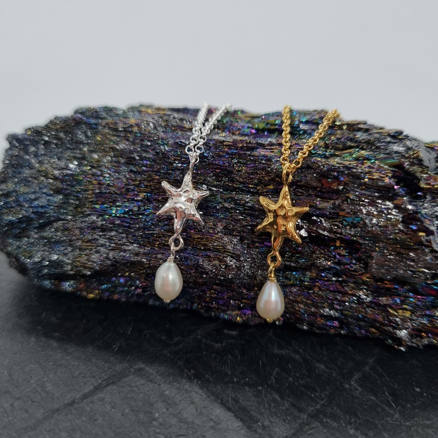 Two star-shaped necklaces with pearl drops on a textured stone surface.