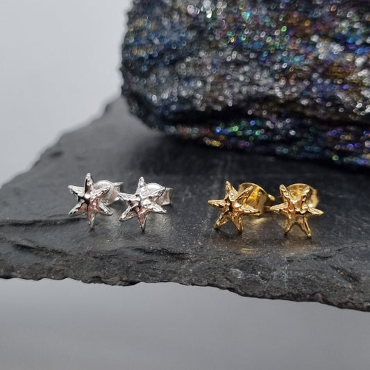 Pair of sterling silver and gold plated star shaped stud earrings on a dark stone surface with a textured fabric background handmade by Jo Cooper