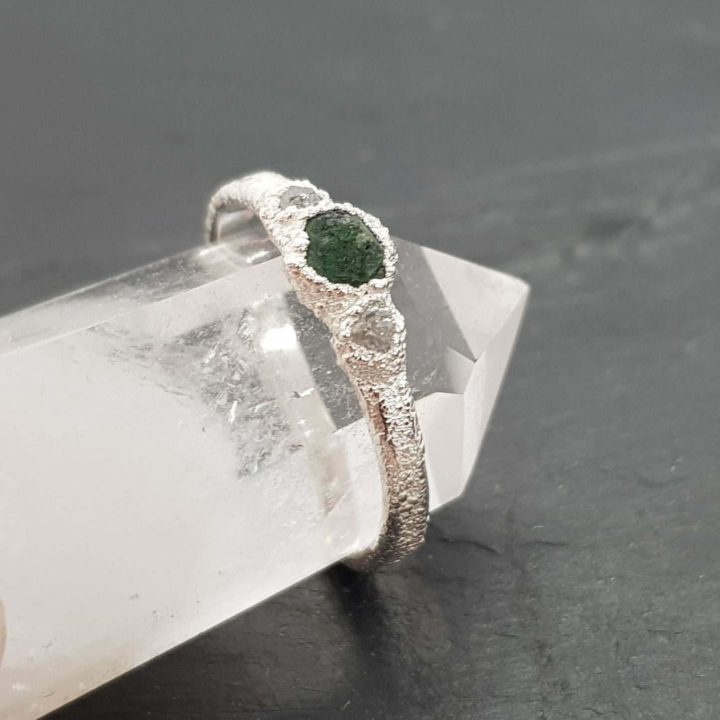 raw emerald and diamond silver ring displayed on a crystal