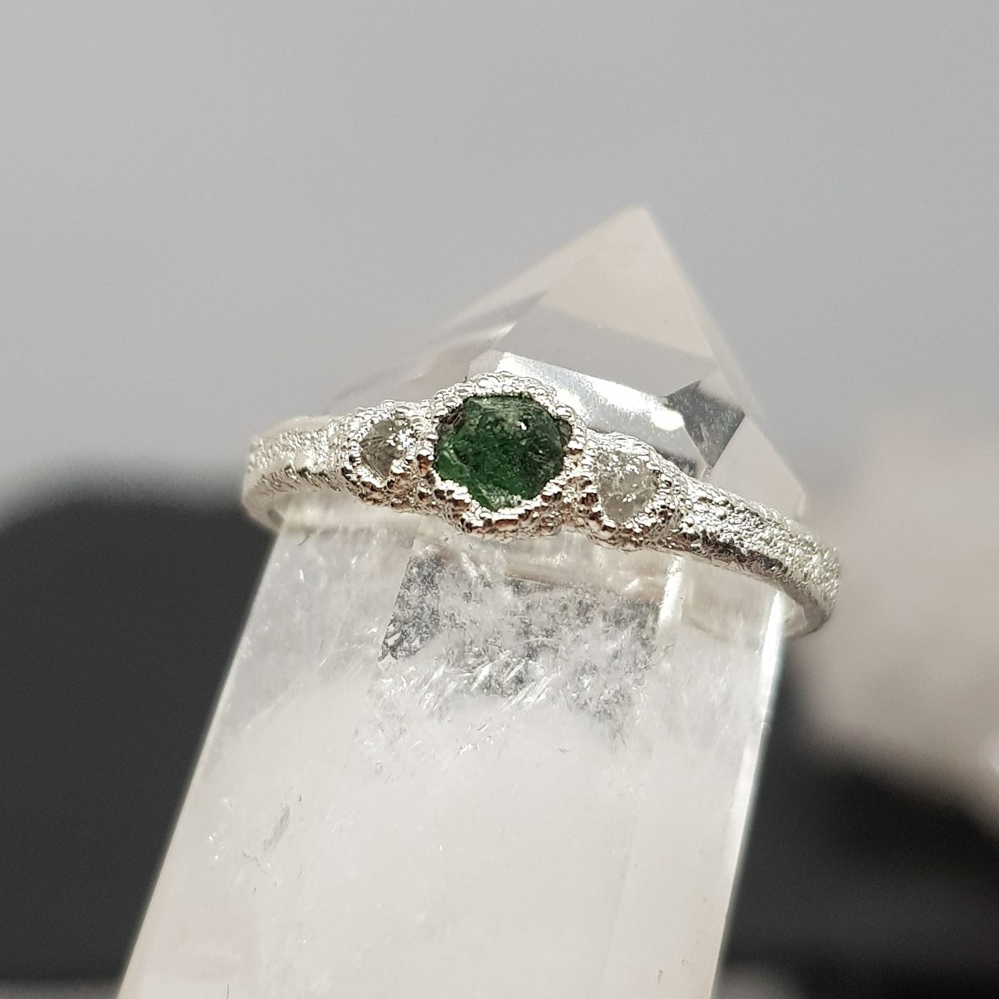 raw emerald and diamond silver ring displayed on a crystal