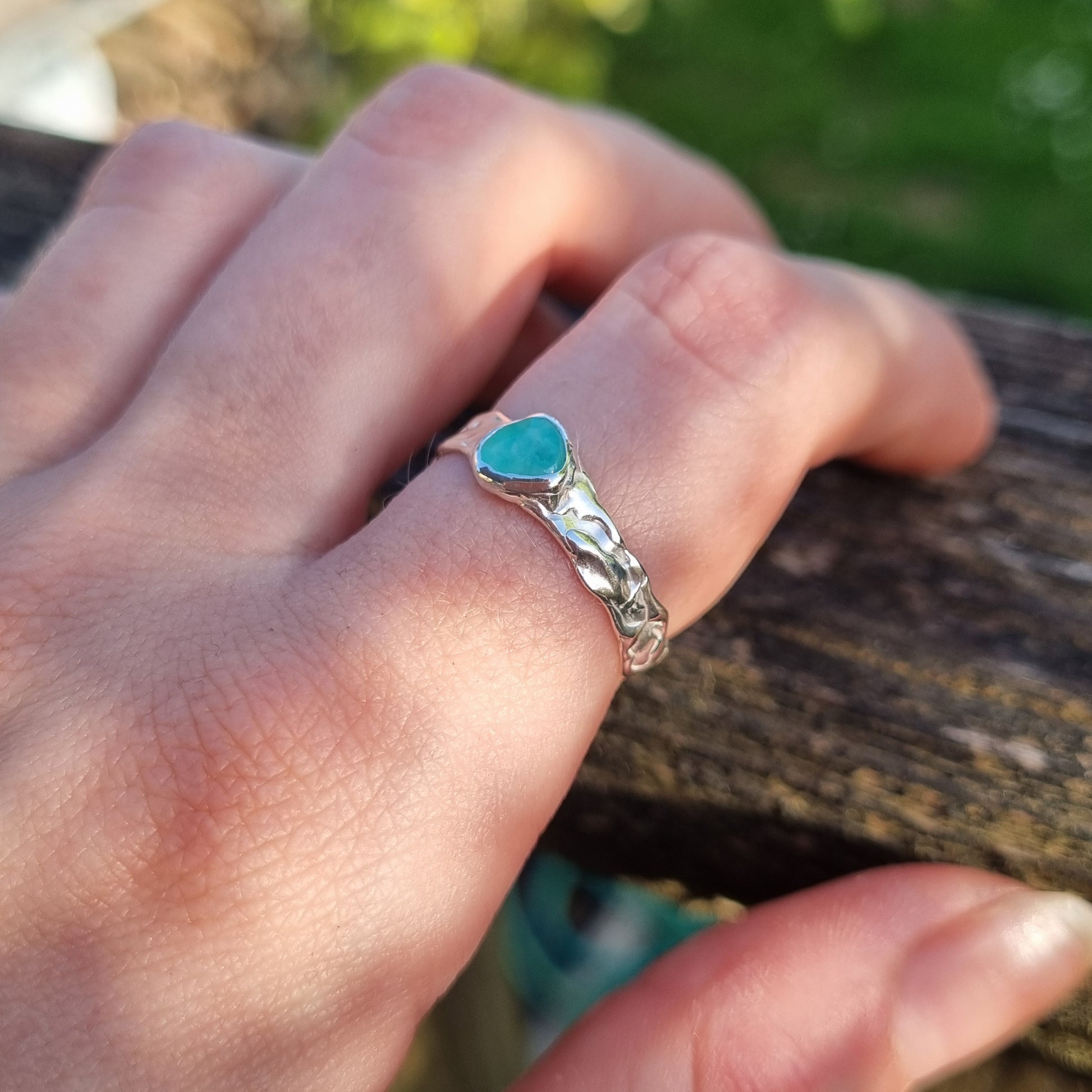 Hand wearing a silver ring with a green gemstone against a blurred natural background