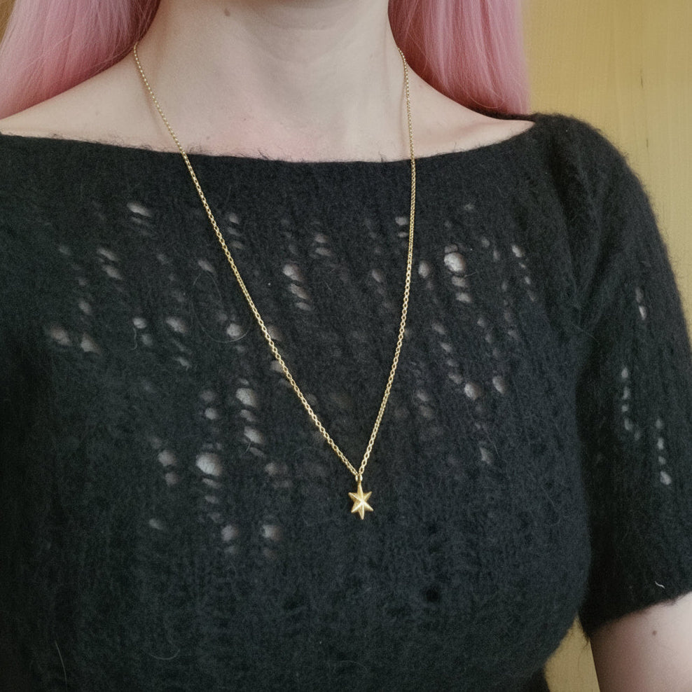 Person wearing a black top with a gold star necklace