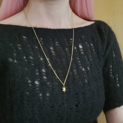 Person wearing a black top with a gold star necklace