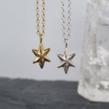 Two star-shaped pendants on sterling silver chains against a neutral background
