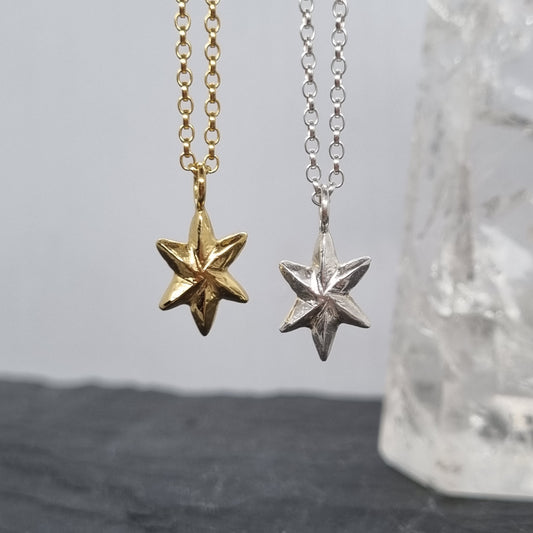 Two star-shaped pendants on sterling silver chains against a neutral background