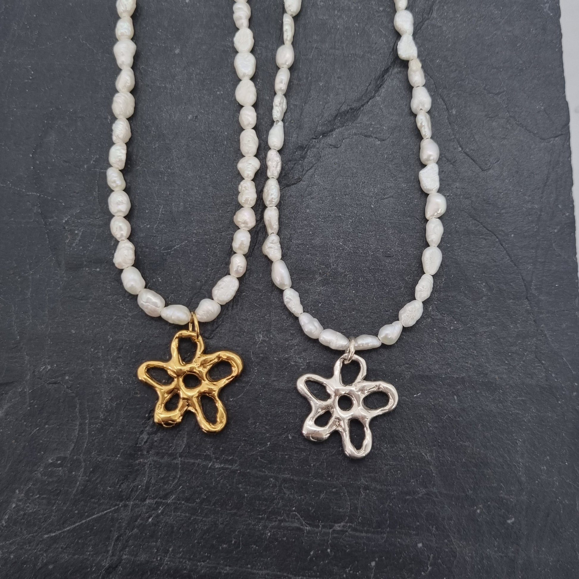 Two pearl beaded necklaces with flower pendants on a dark stone surface