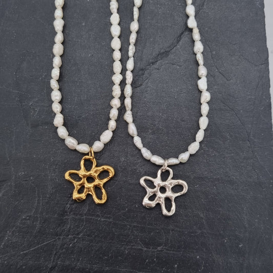 Two pearl beaded necklaces with flower pendants on a dark stone surface