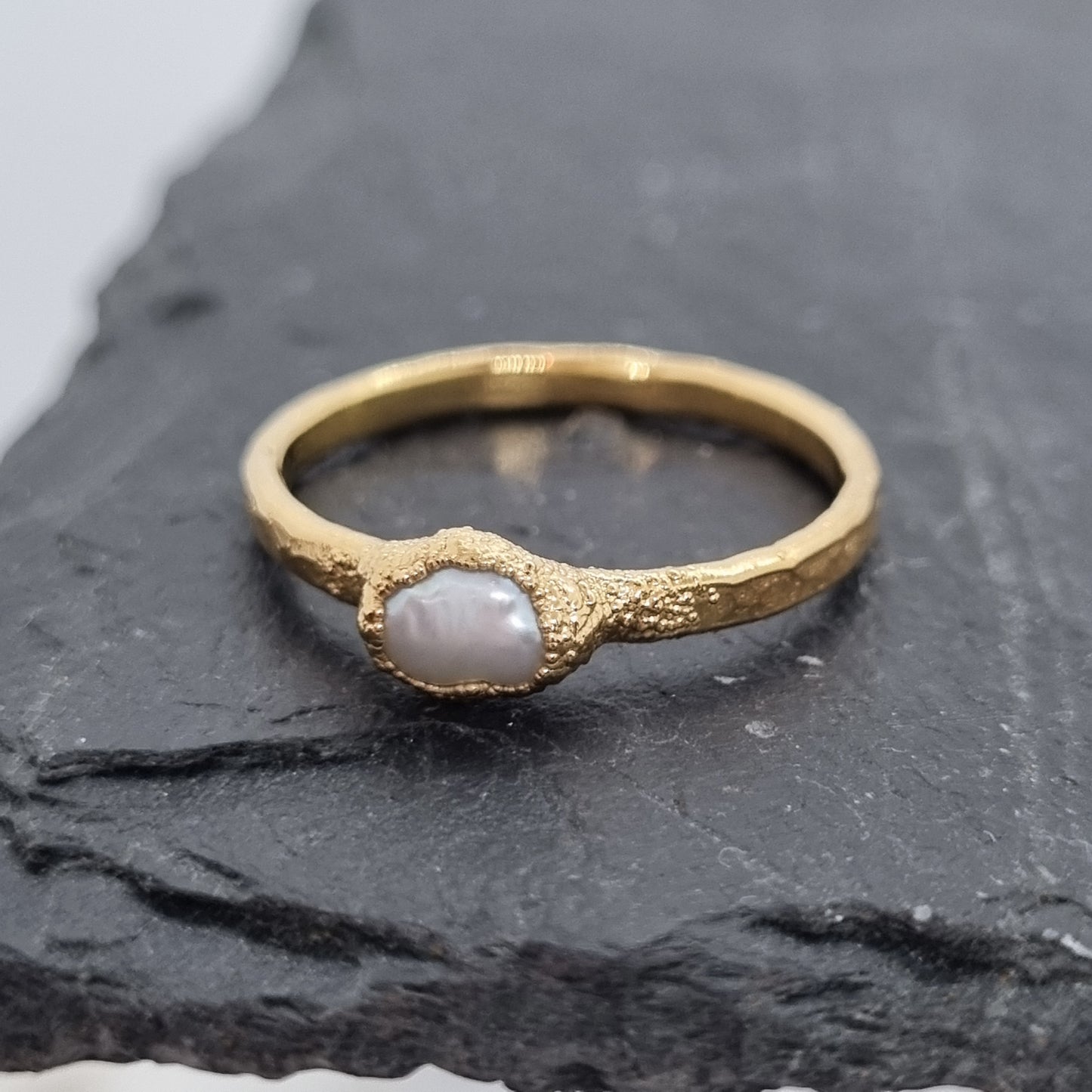 Gold ring with a freshwater pearl on a dark stone surface