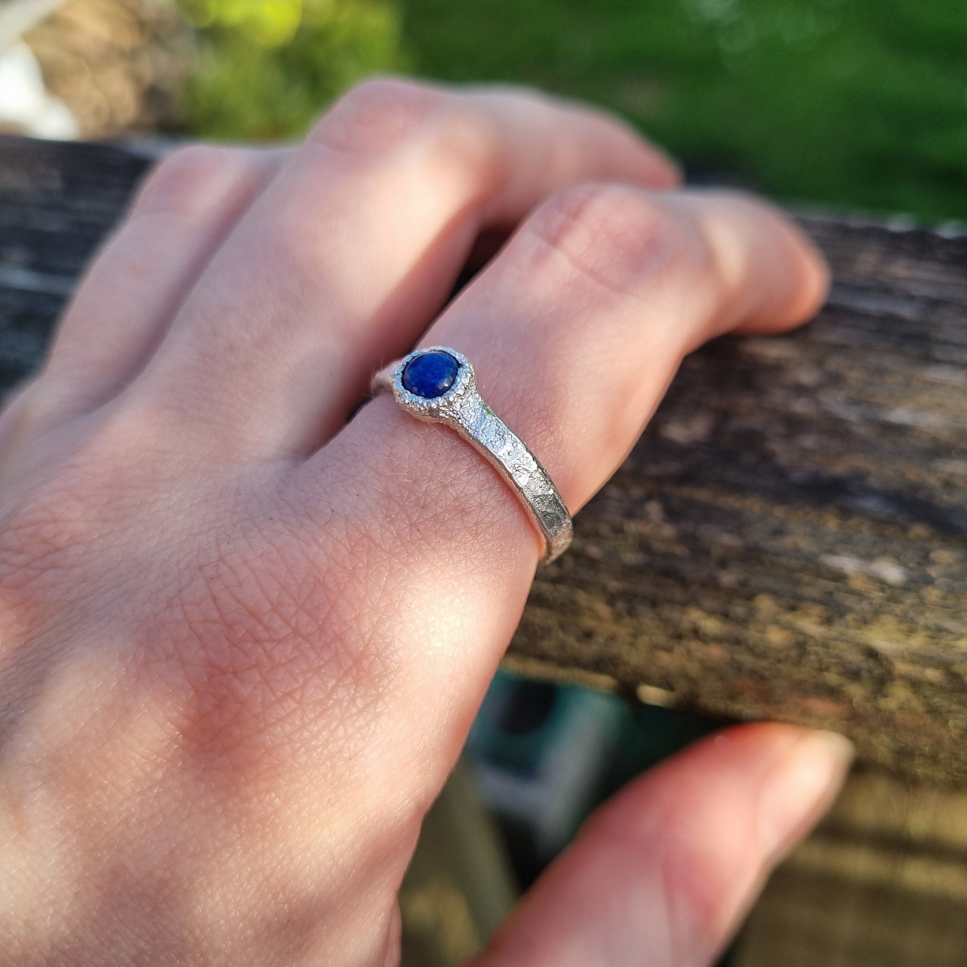 Hand wearing a silver ring with lapis lazuli gemstone against a natural background