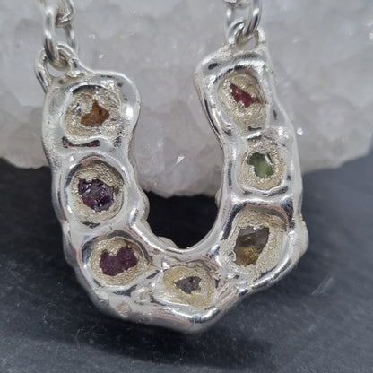 close up of the back of a sterling silver horseshoe pendant necklace with colourful raw natural gemstones set in it