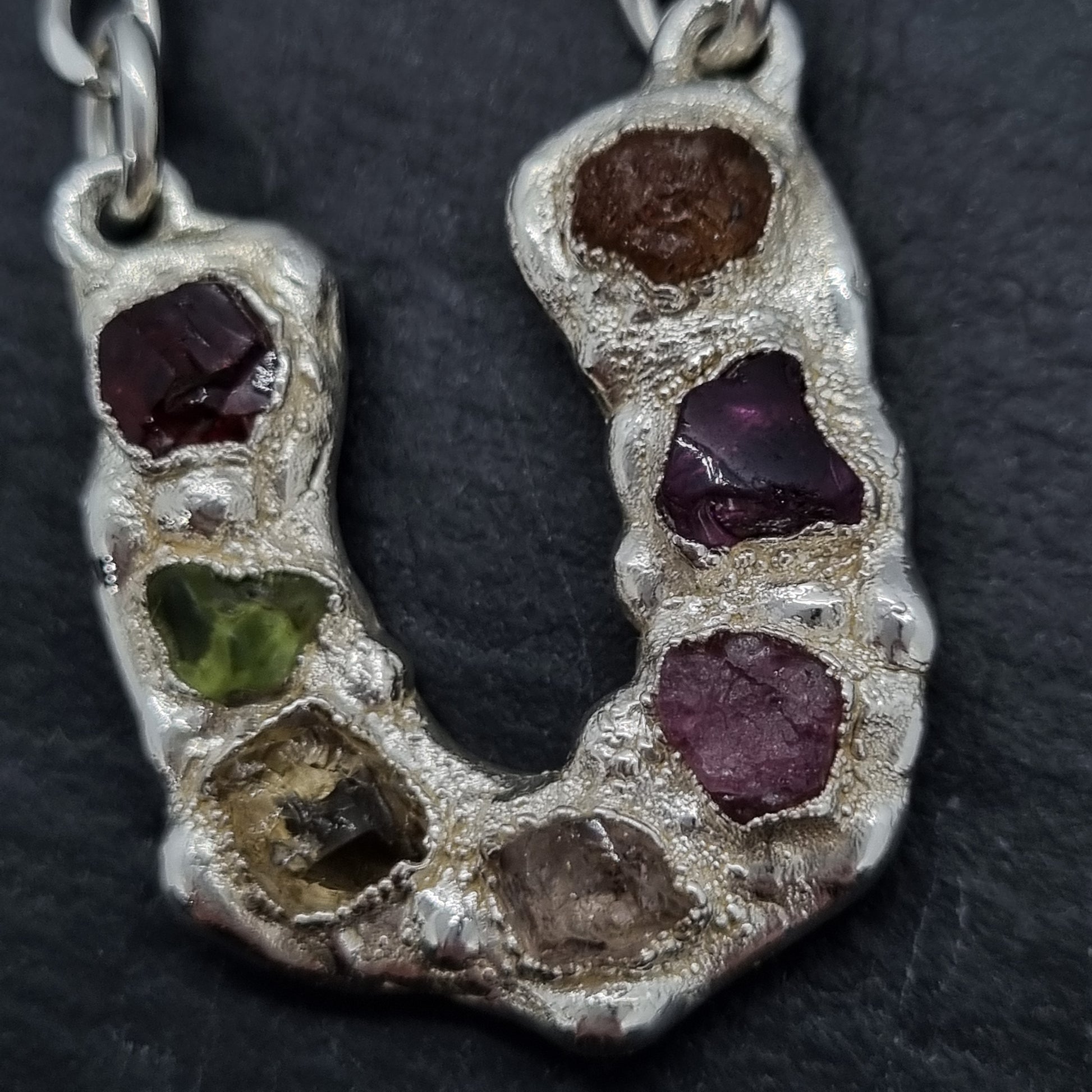 Sterling silver horseshoe pendant necklace with multi coloured raw natural gemstones, including red garnet, peridot, citrine, morganite, pink tourmaline, rhodolite garnet, and mandarin garnet.