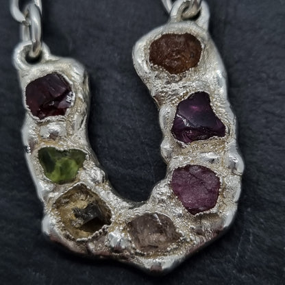 Sterling silver horseshoe pendant necklace with multi coloured raw natural gemstones, including red garnet, peridot, citrine, morganite, pink tourmaline, rhodolite garnet, and mandarin garnet.