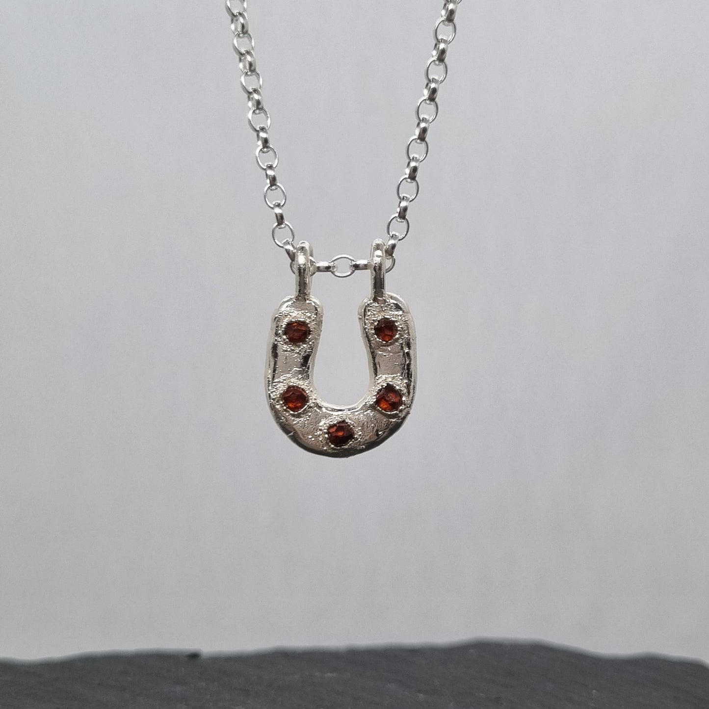 Sterling silver horseshoe necklace with five embedded spessartite garnet crystal gemstones set in it. The silver has a texture to it. Handmade by Jo Cooper Jewellery