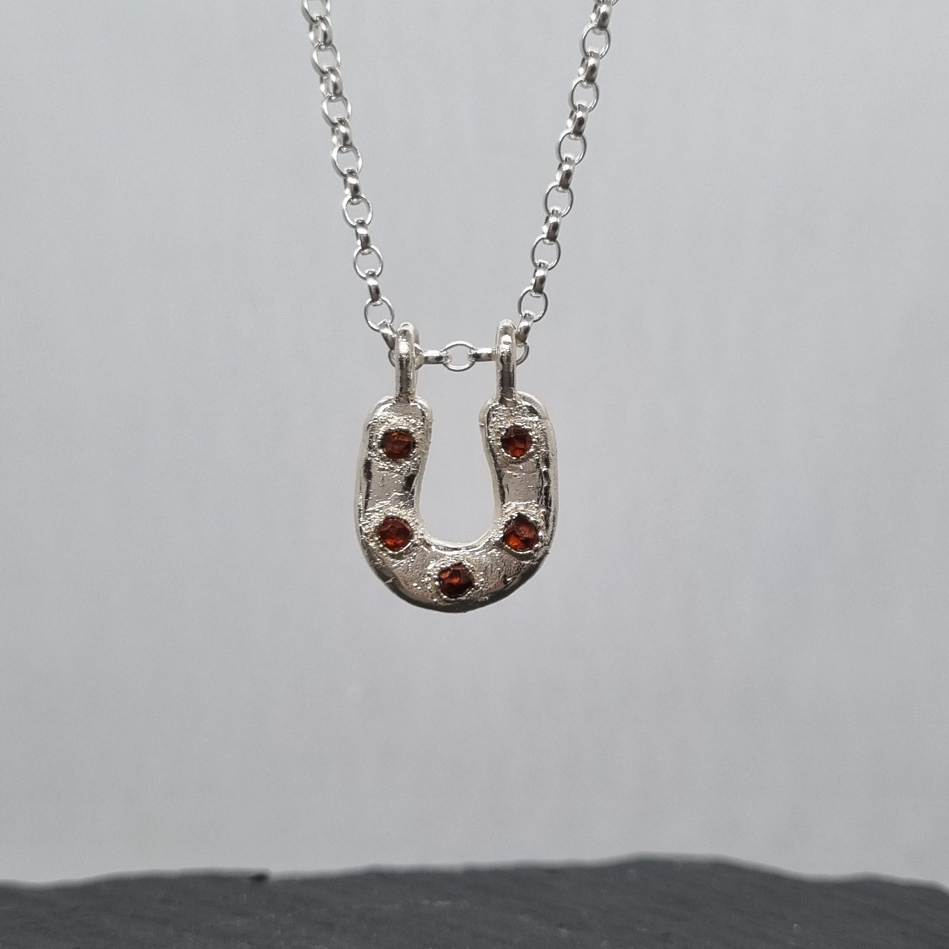 Sterling silver horseshoe necklace with five embedded spessartite garnet crystal gemstones set in it. The silver has a texture to it. Handmade by Jo Cooper Jewellery