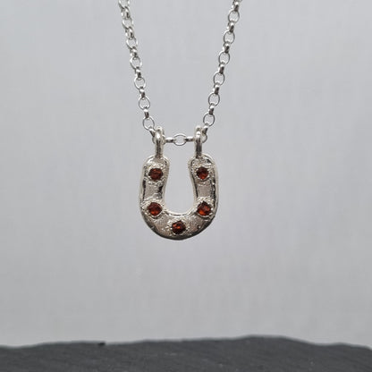 Sterling silver horseshoe necklace with five embedded spessartite garnet crystal gemstones set in it. The silver has a texture to it. Handmade by Jo Cooper Jewellery