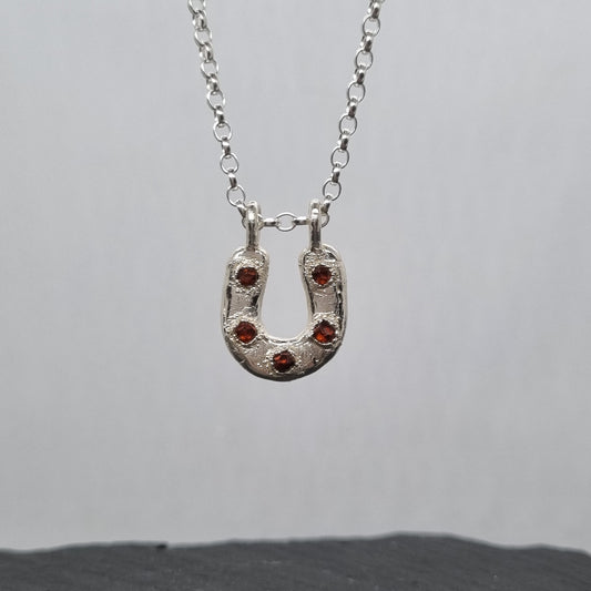 Sterling silver horseshoe necklace with five embedded spessartite garnet crystal gemstones set in it. The silver has a texture to it. Handmade by Jo Cooper Jewellery