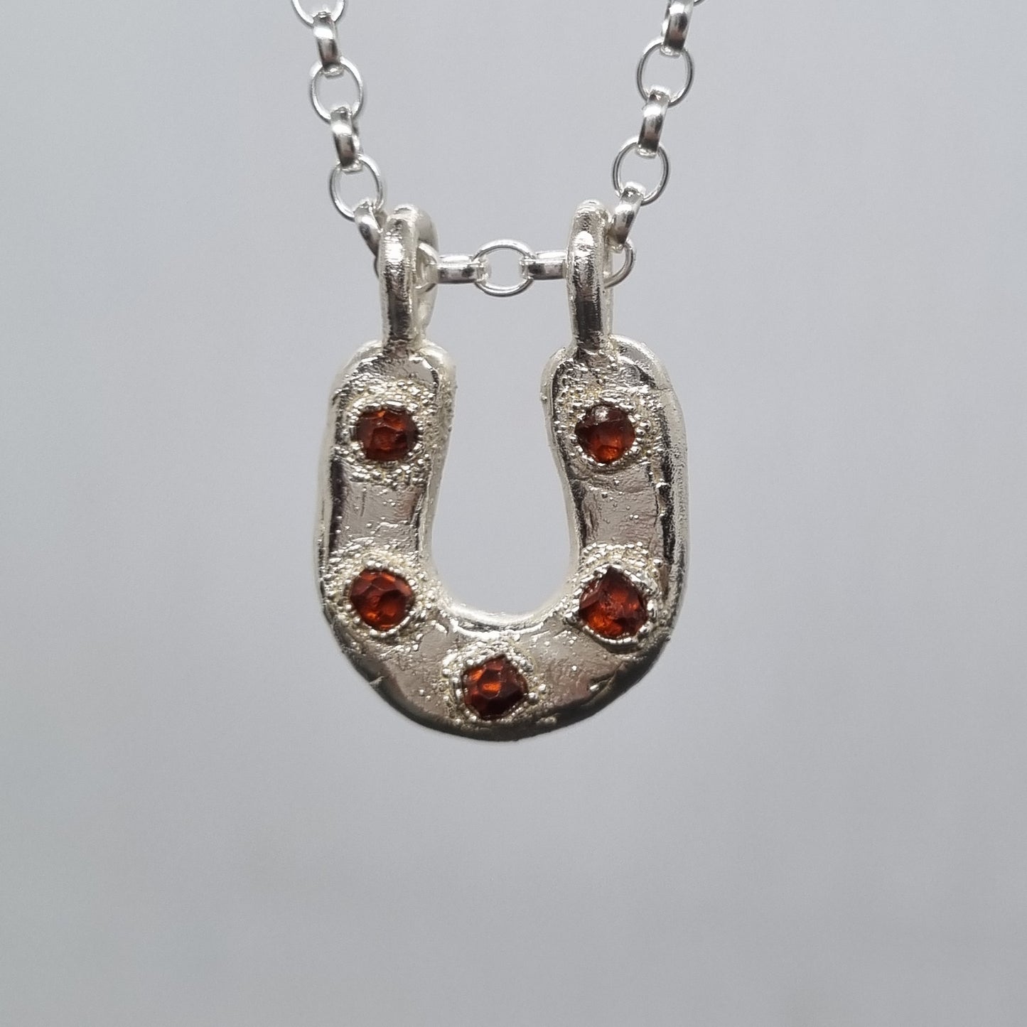 Sterling silver horseshoe necklace with orange spessartite garnet crystals set in it. Electroformed silver texture