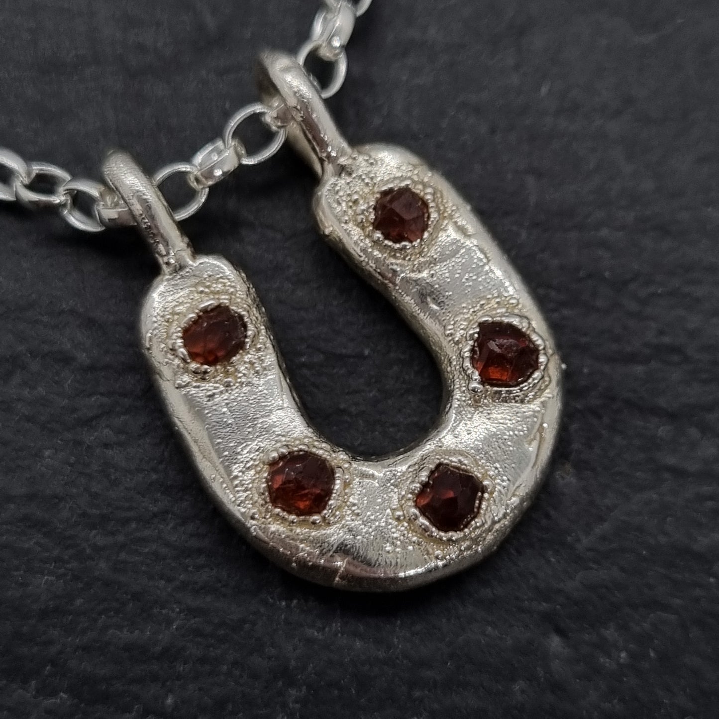 Sterling silver horseshoe necklace with five raw orange spessartite garnets set in it. The silver has a texture to it. Lunar New Year of the Horse Collection