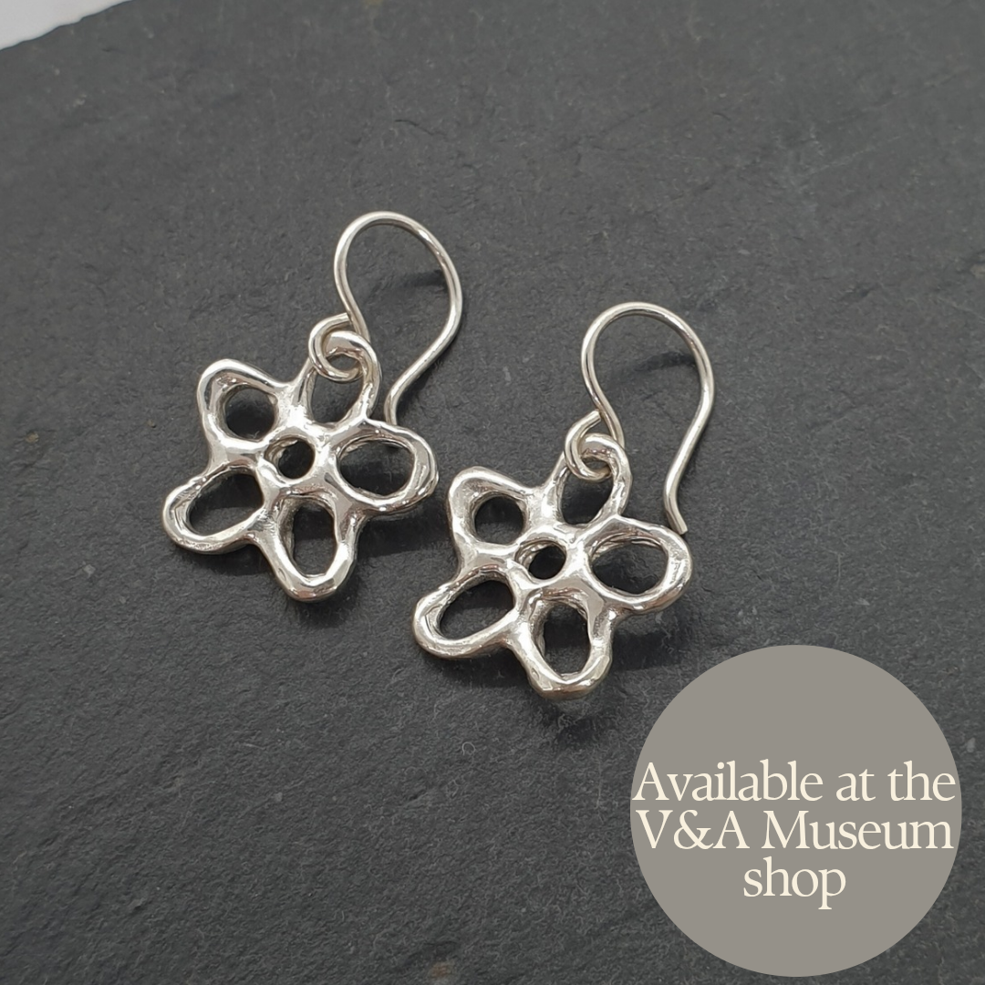 Silver flower-shaped earrings on a dark background with 'Available at the V&A Museum shop' text.