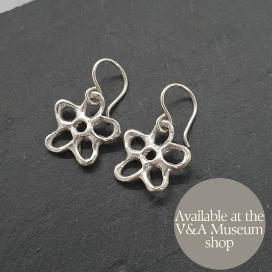 Silver flower-shaped earrings on a dark background with 'Available at the V&A Museum shop' text.