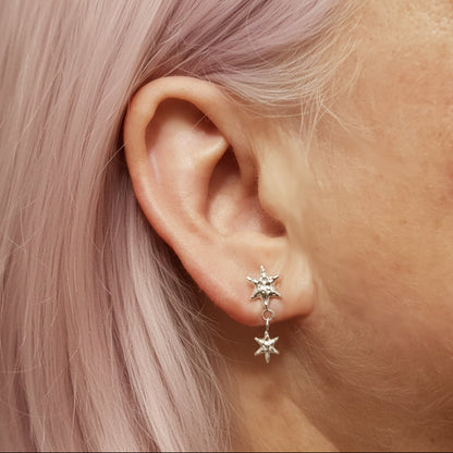 Star-shaped earrings worn by a person with light pink hair.