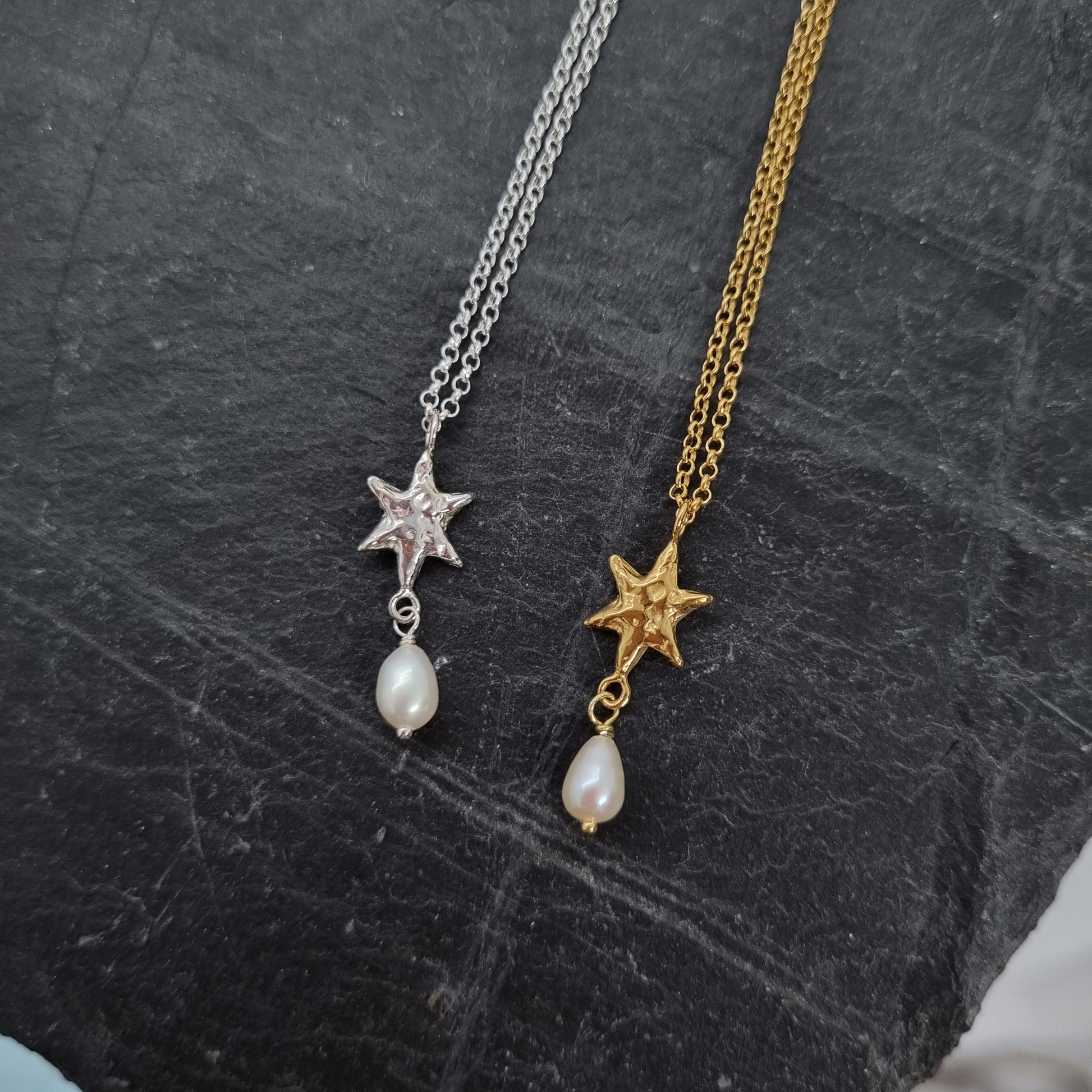 Two star-shaped pendants on gold and silver chains against a dark textured background