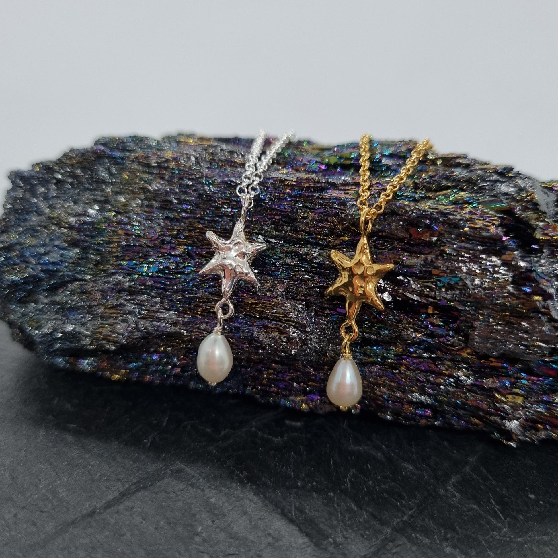 Two star-shaped necklaces with pearl drops on a textured stone surface.