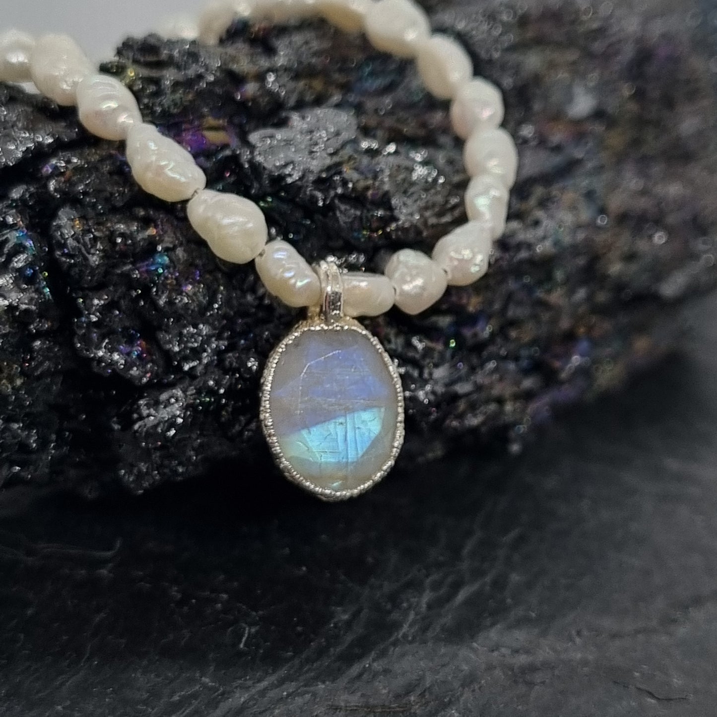 sterling silver pearl necklace with a rainbow moonstone pendant on a dark stone background