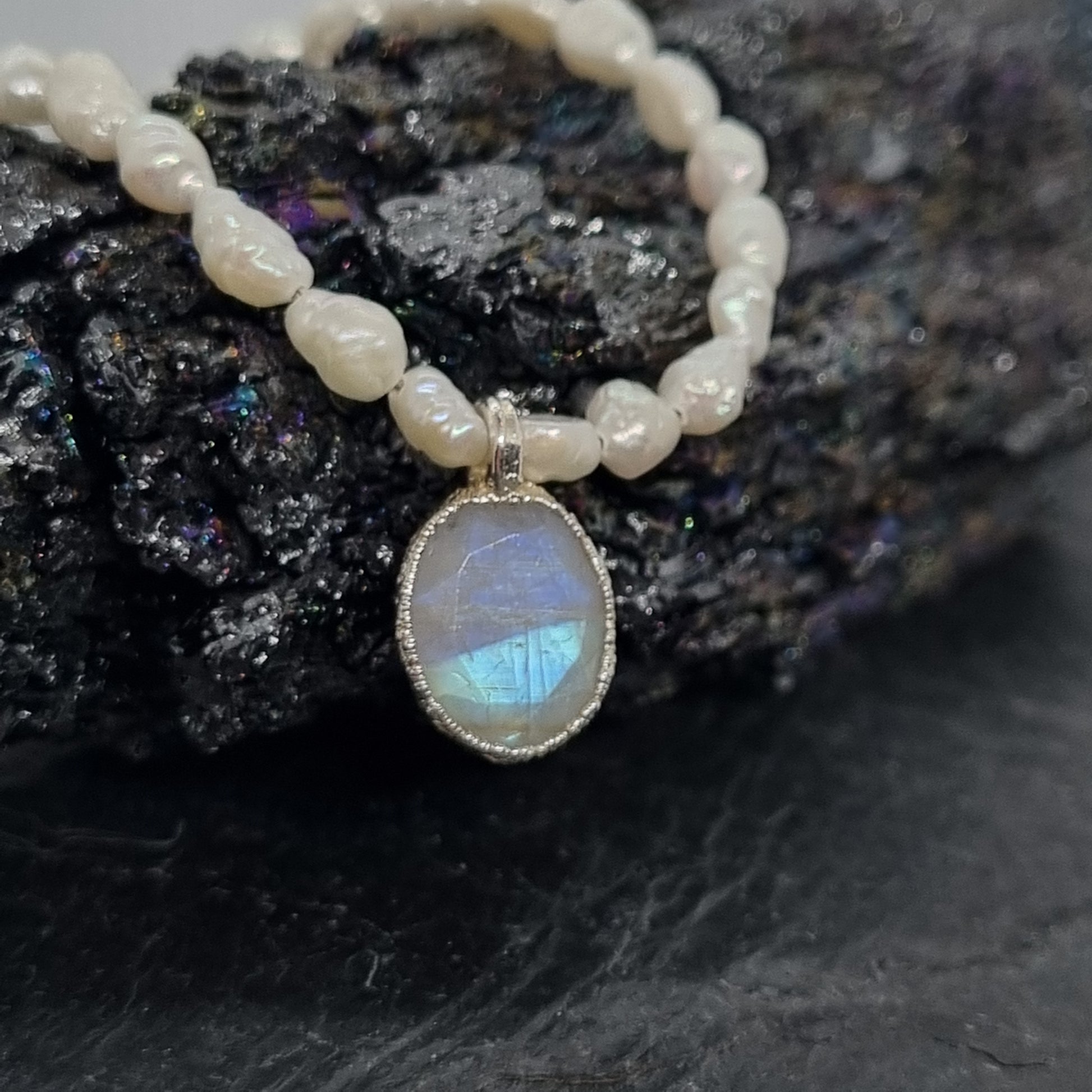 sterling silver pearl necklace with a rainbow moonstone pendant on a dark stone background