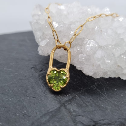Gold necklace with green peridot gemstone pendant on a dark surface with white crystal background