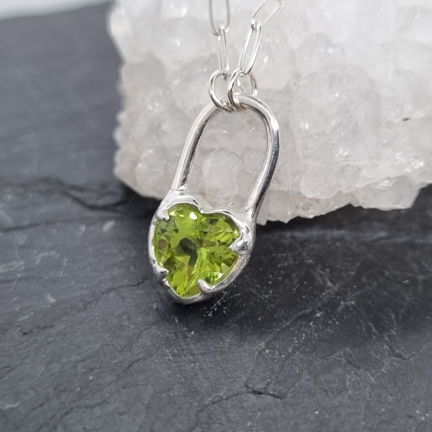 heart-shaped green peridot gemstone pendant on silver chain against a crystal