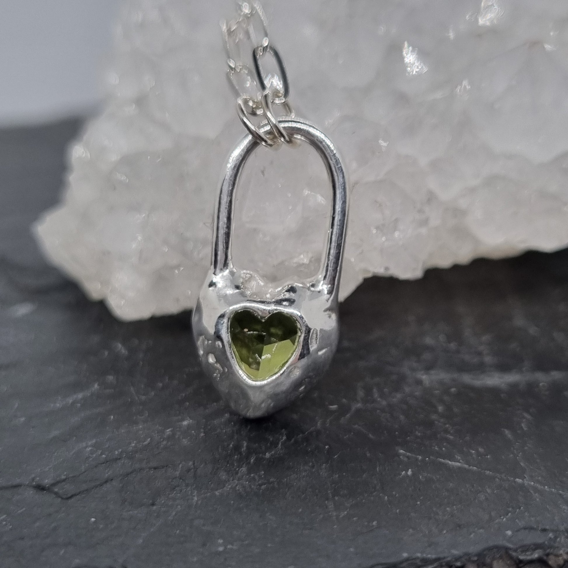 heart lock sterling silver pendant with a green gemstone on a dark surface