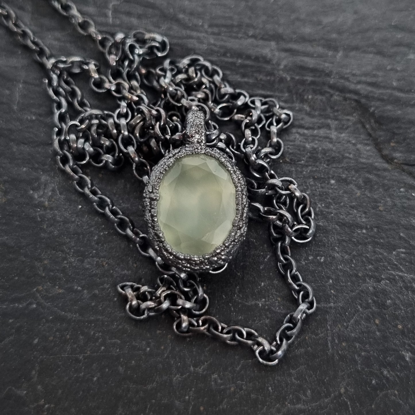 Necklace with a green stone pendant on a dark textured surface