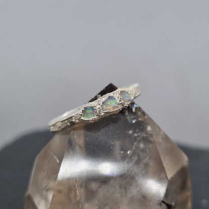 A fine silver ring with three freeform opal gemstones, shown close-up against a soft grey background with a translucent crystal prop.