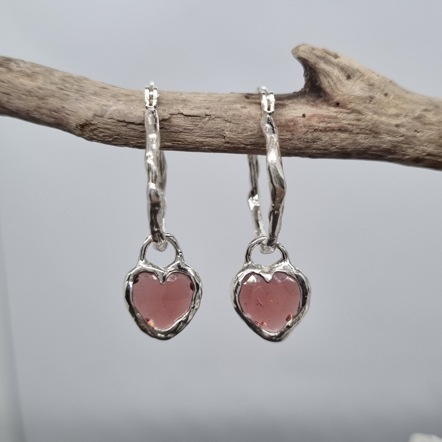 Heart-shaped earrings with rose cut red garnet gemstones hanging from a branch against a gray background