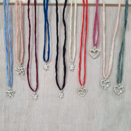 Silk cord necklaces with various sterling silver pendants on a wooden surface