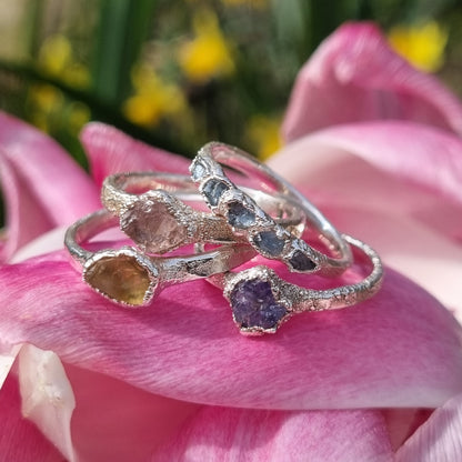 a stack of raw gemstone silver rings displayed on a pile of Spring pink tulip petals