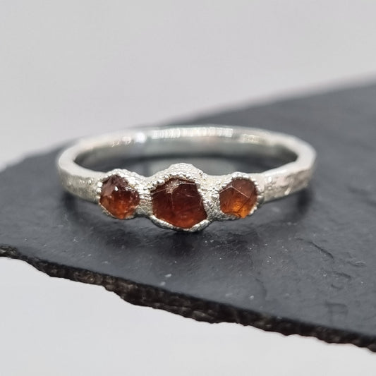 Fine Silver ring with embedded spessartite garnet raw stones on a dark stone surface