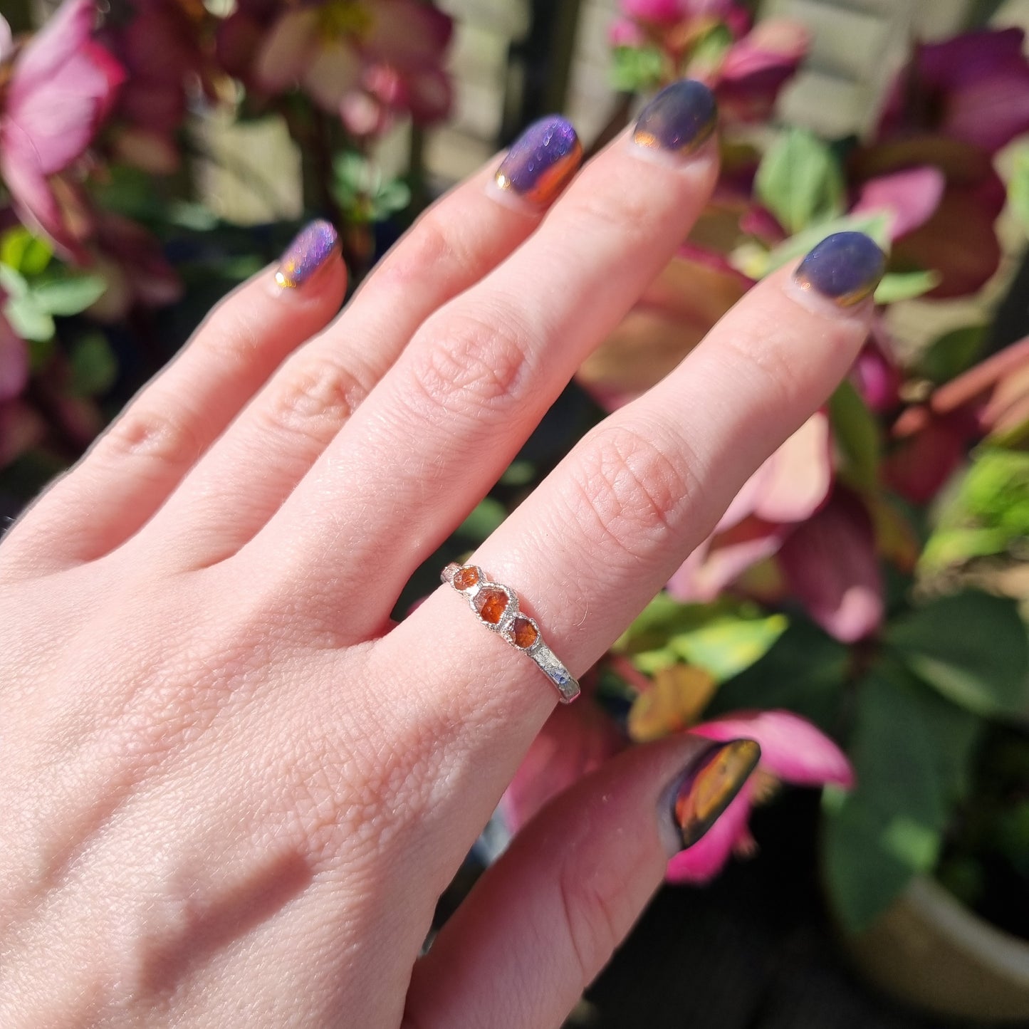 Hand with a silver ring featuring raw spessartite garnet gemstones against a floral background