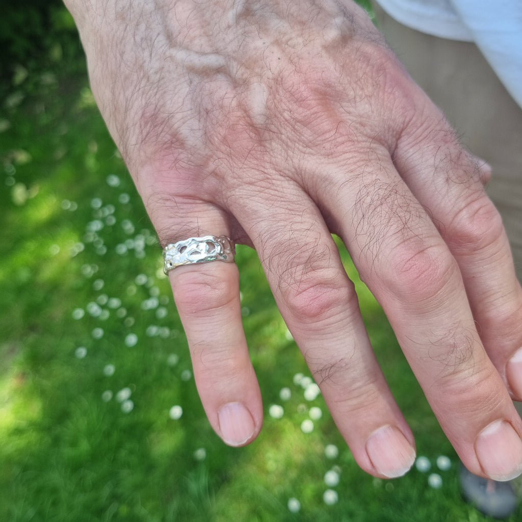 Hand wearing a molten sterling silver ring with a blurred green background