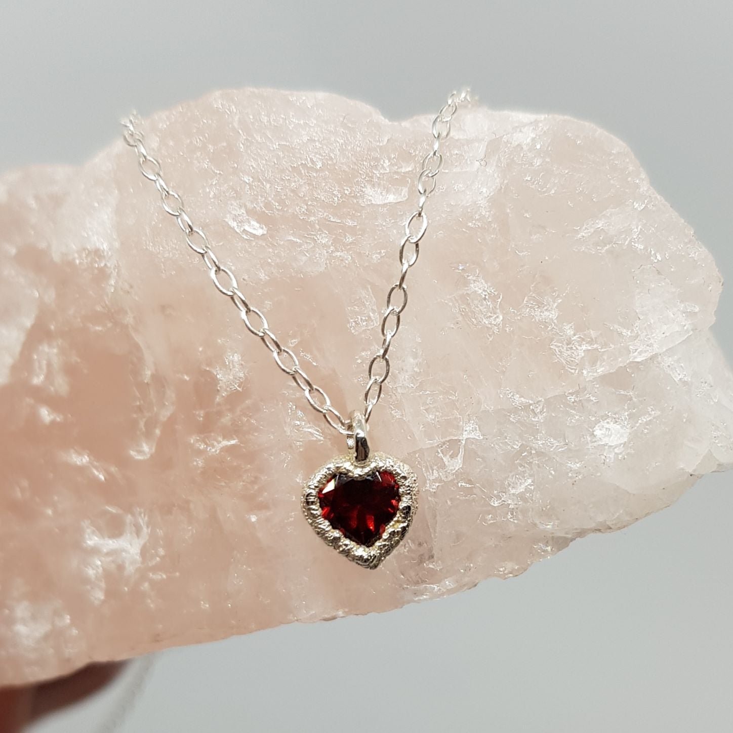 raw silver garnet heart silver necklace displayed on a piece of rose quartz