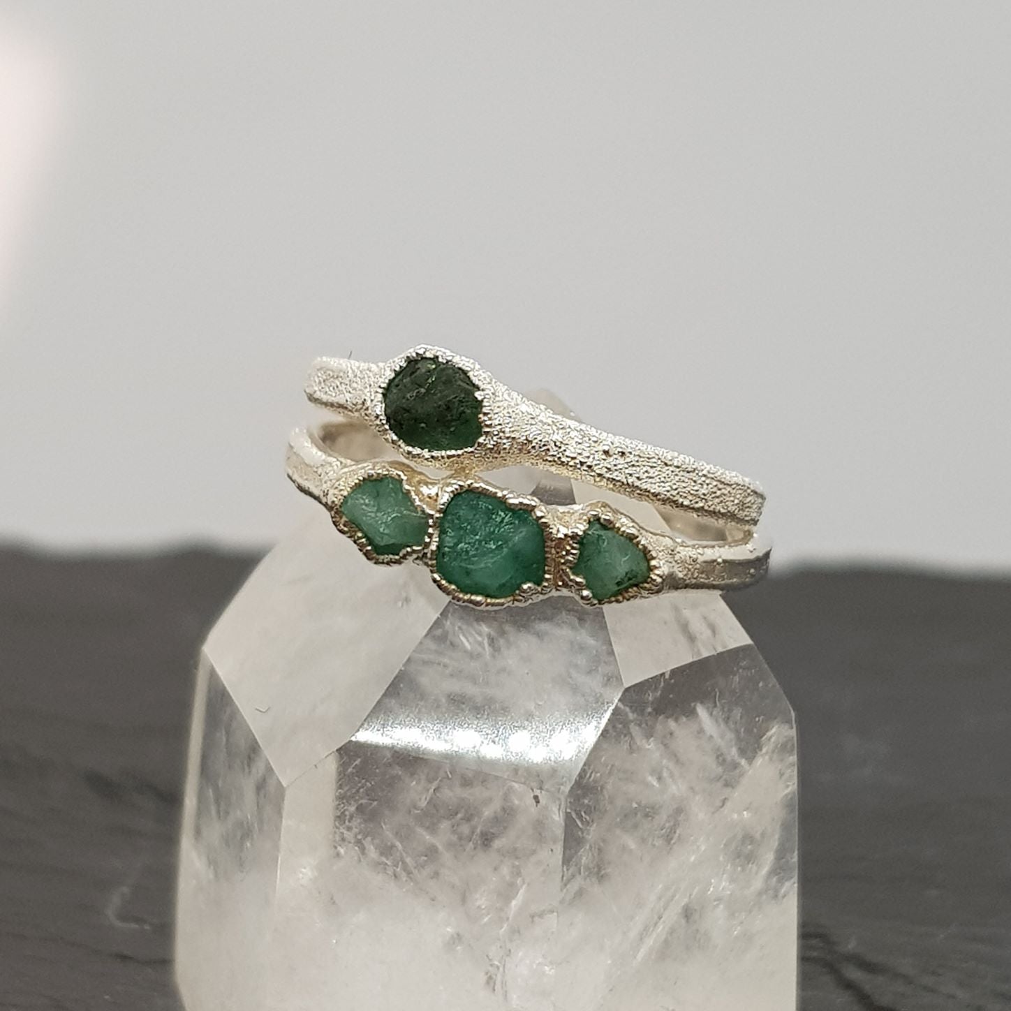 single and triple raw emerald silver ring displayed on a crystal