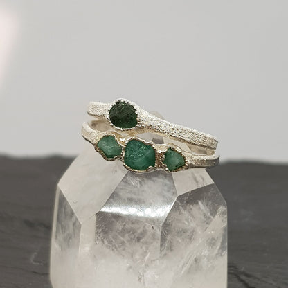 single and triple raw emerald silver ring displayed on a crystal